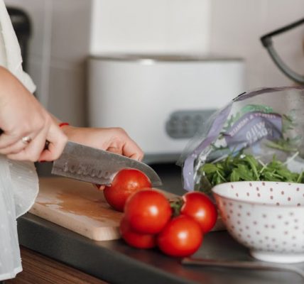 Crop anonymous housewife in casual clothes cutting fresh ripe tomatoes with sharp knife on wooden cutting board while cooking in kitchen